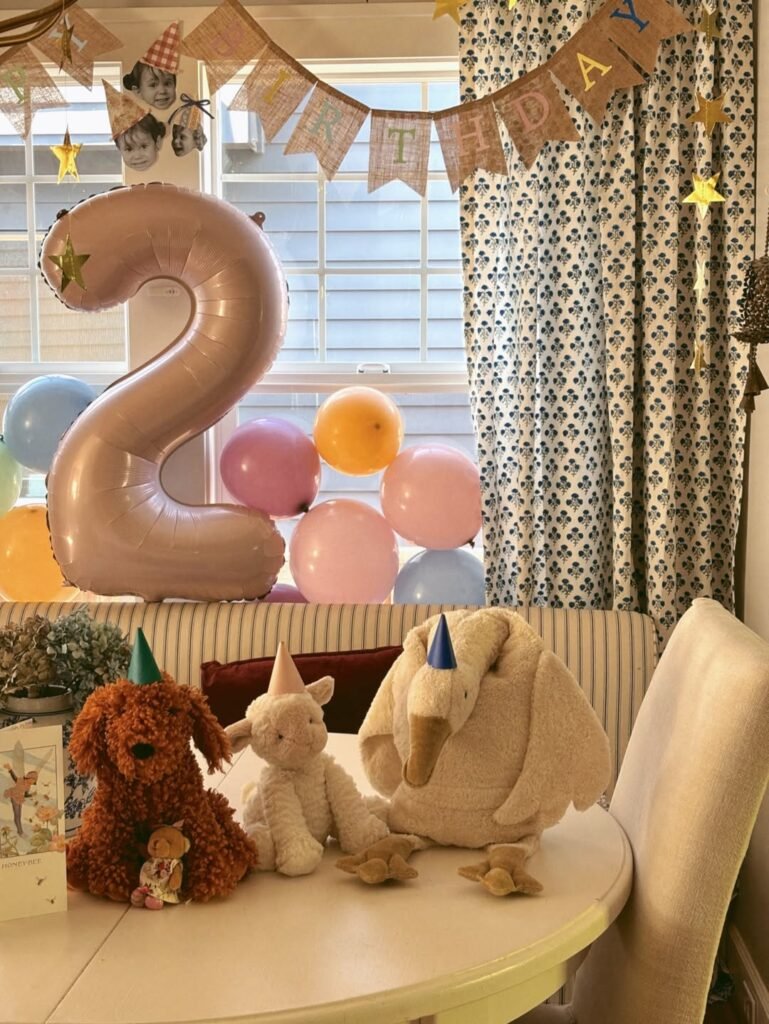 Big 2 foil balloon behind plush toys wearing party hats on a white table for a 2nd birthday