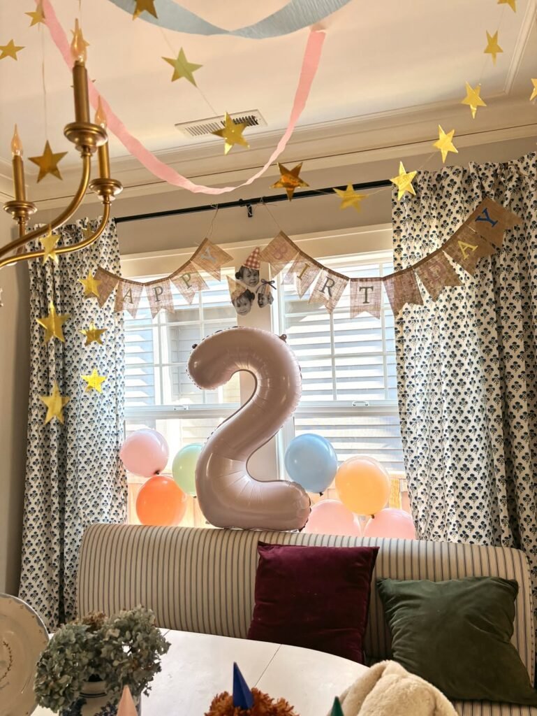 Window seat balloon backdrop with a big 2 balloon, pastel balloons, bunting and gold star garland for a 2nd birthday