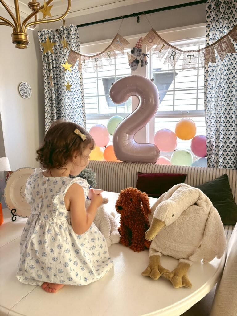 Birthday girl looking at plush animals on the table under gold stars and streamers