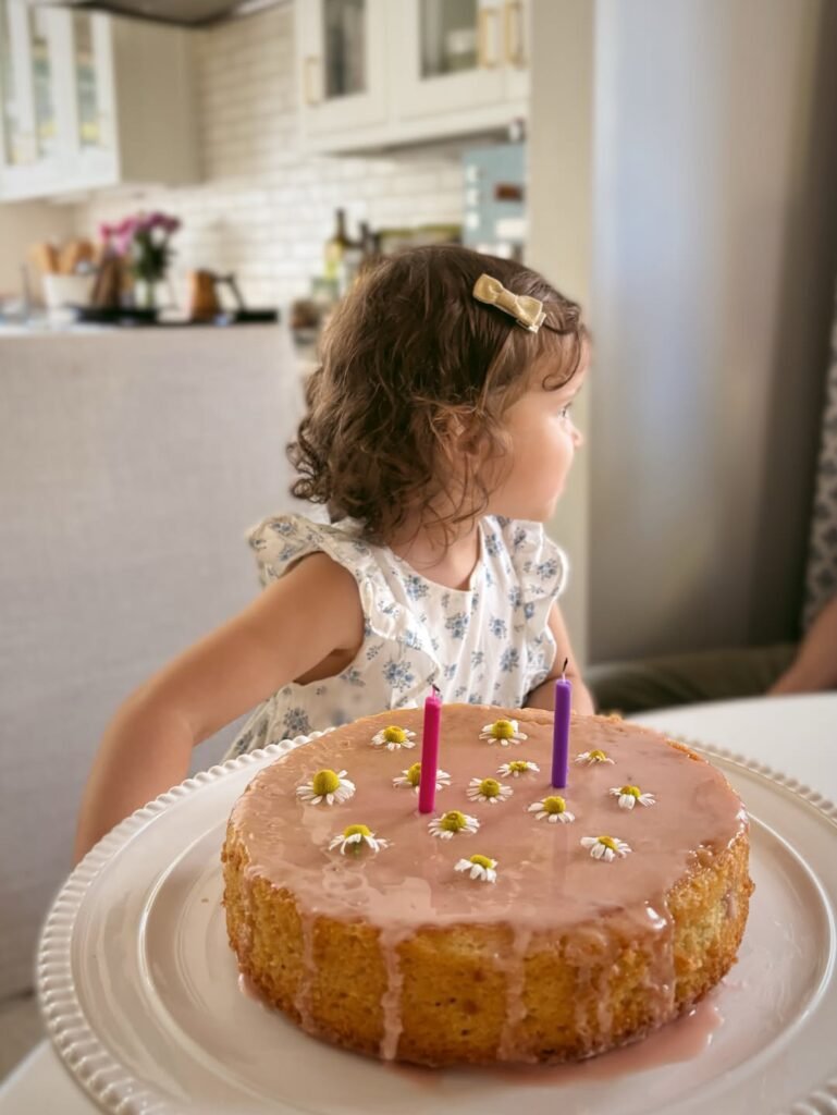 Birthday girl looking at a simple glazed cake with pink candles