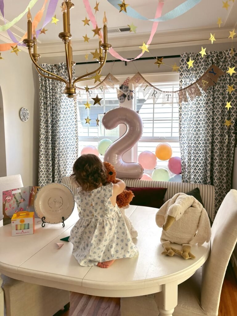 Birthday girl standing on the table by a pink number 2 balloon under streamers
