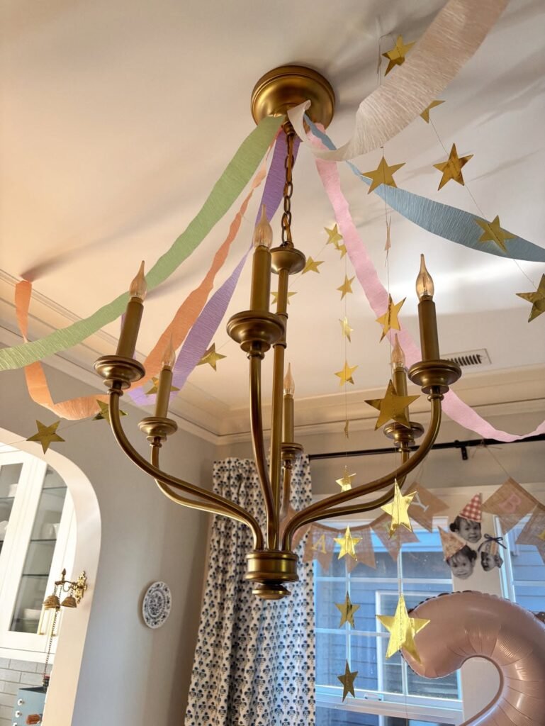 Brass chandelier wrapped with gold star garland and pastel ribbon streamers for a 2nd birthday party