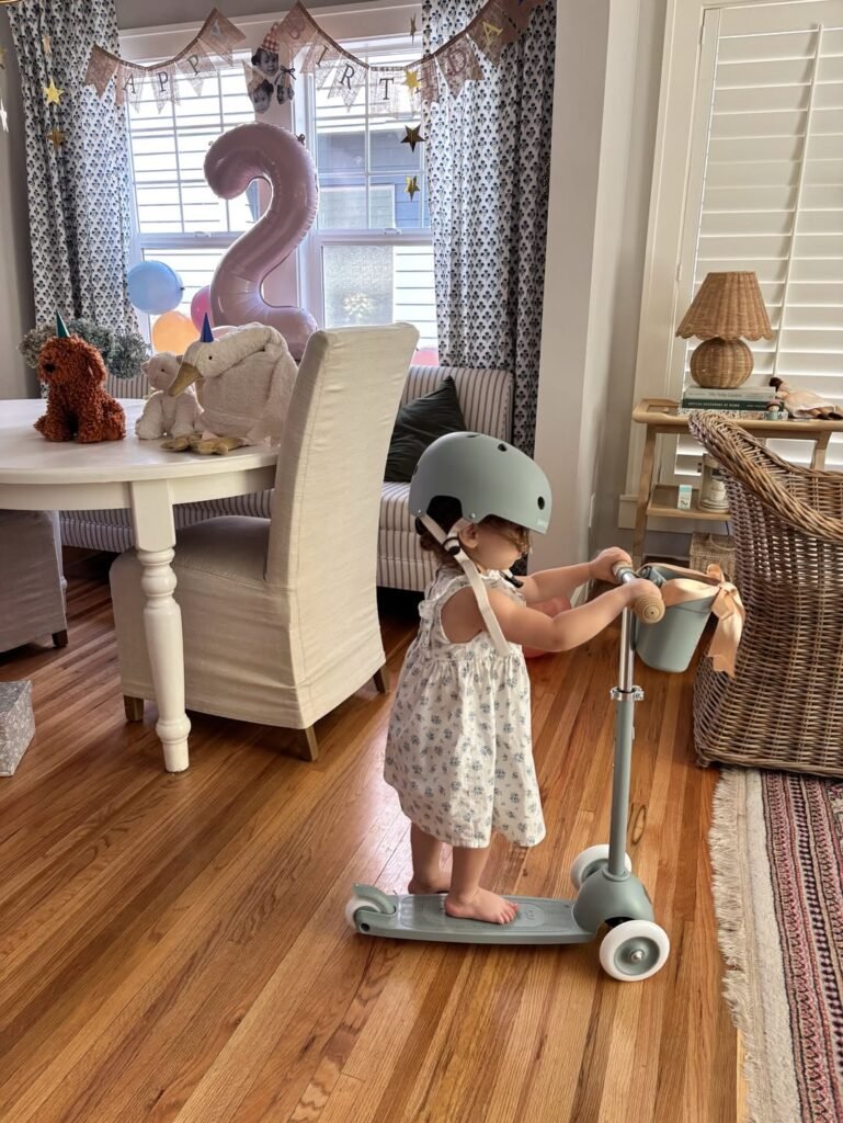 Toddler in a helmet riding a new scooter at a 2nd birthday party at home