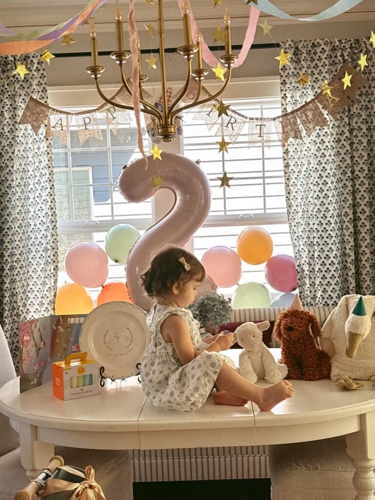 Birthday girl sitting on the table with a pink number 2 balloon and teddy bears