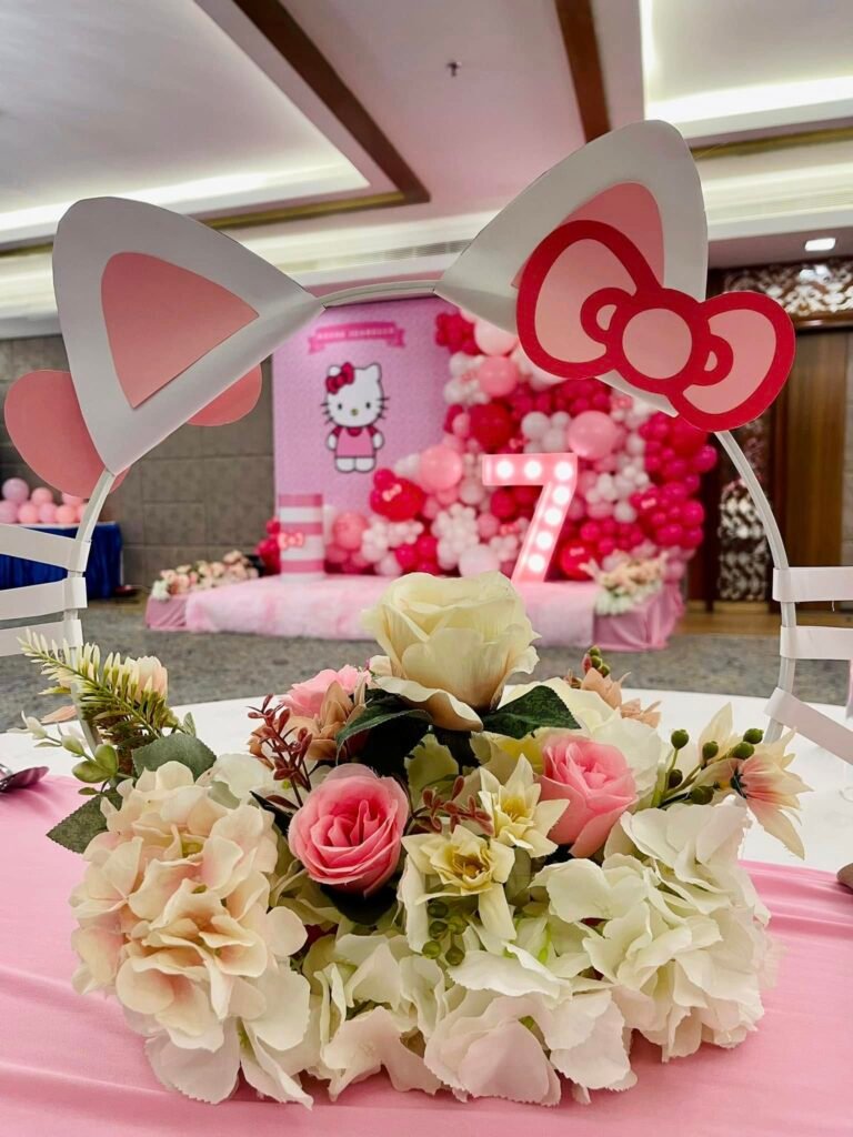 Floral centerpiece with pink roses and hydrangeas under a white Hello Kitty ear and bow frame