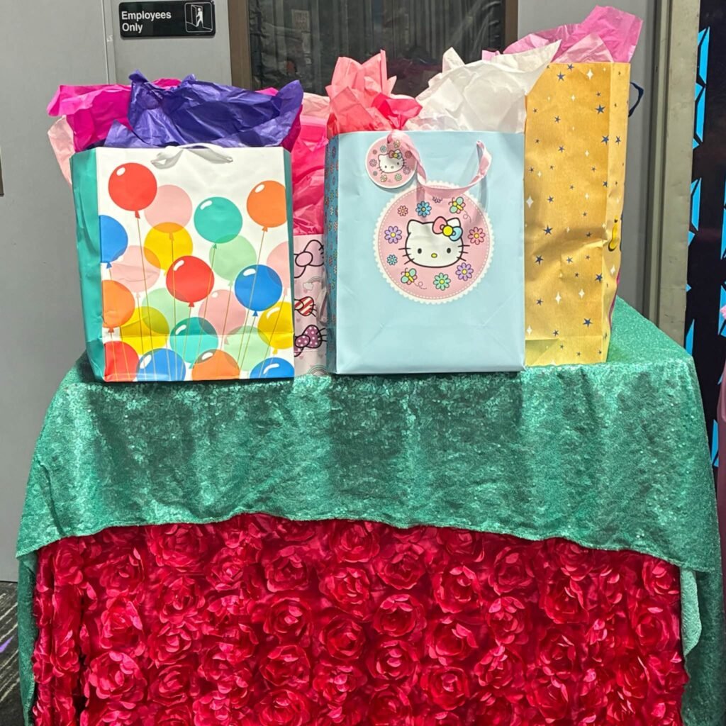 Gift table with a red rosette tablecloth, a teal overlay and gift bags with Hello Kitty tags