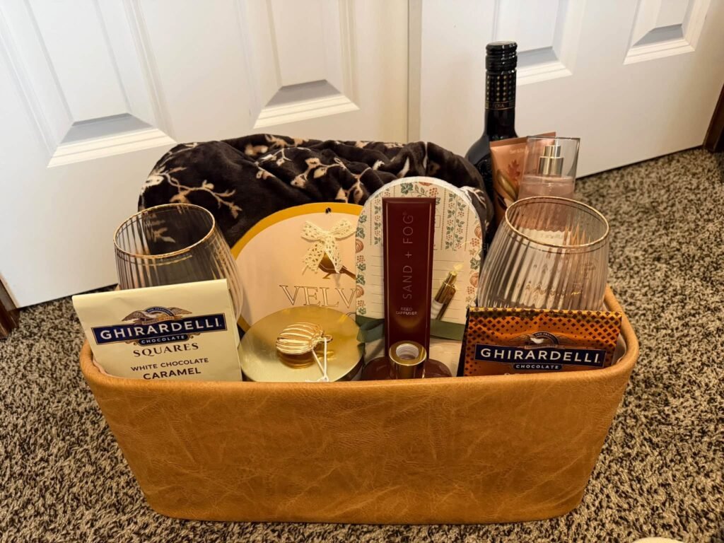 Fall gift basket with a wine bottle, glasses, a candle, Ghirardelli chocolate and a throw blanket in a leather look basket