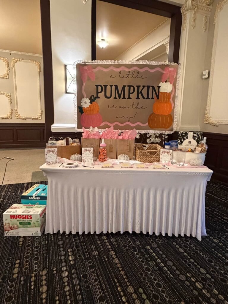 Baby shower table under a pink A Little Pumpkin Is on the Way sign with gift bags, candy jars and diaper boxes