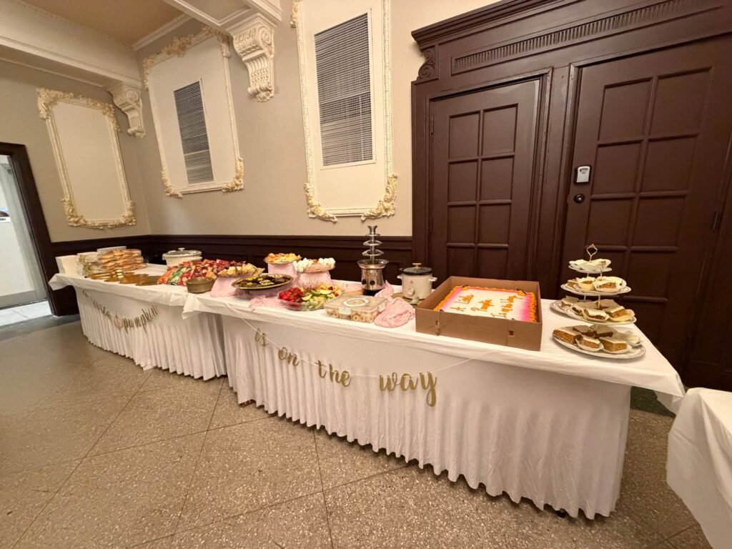 Baby shower dessert and snack buffet with trays, cake stands and an On the Way script garland on a white table