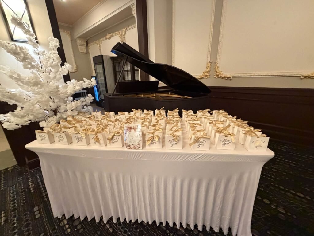 Baby shower favor table with rows of white and gold favor boxes next to a white blossom tree