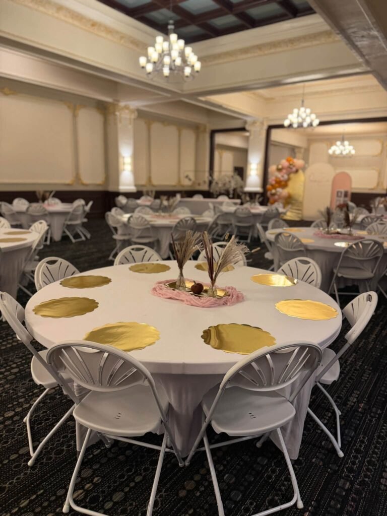 Ballroom baby shower tables with white cloths, gold scalloped chargers, white chairs and pampas centerpieces