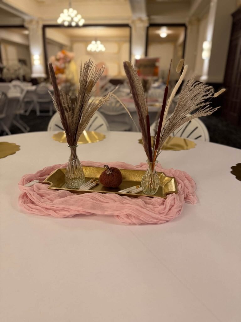 Pampas grass centerpiece in gold bud vases on a gold tray with a small pumpkin and pink cheesecloth