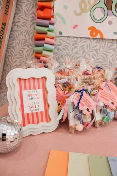 Craft favor bags with pastel ribbons next to a wavy frame thank you sign and a disco ball