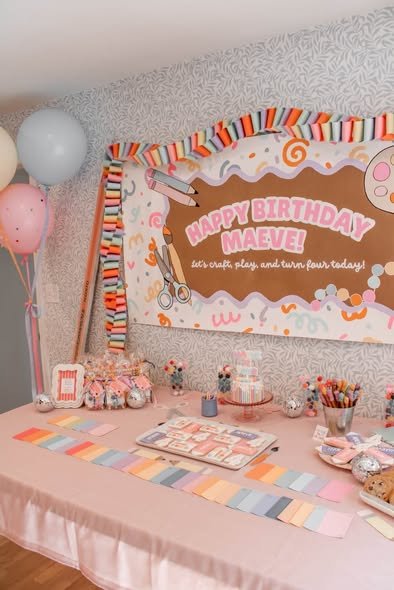 Arts and crafts birthday backdrop with a Happy Birthday sign, squiggle border, rainbow paper chains and a paint swatch table runner