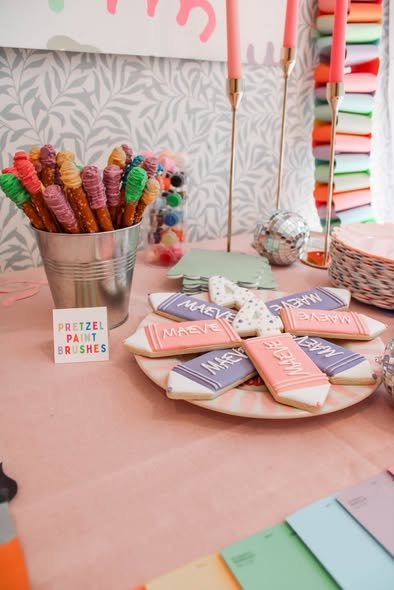 Pretzel rods dipped in candy melts and sprinkles to look like paint brushes in a metal bucket