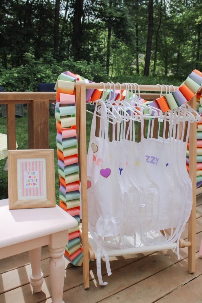 Wooden clothes rack with white kids art aprons and rainbow paper chains
