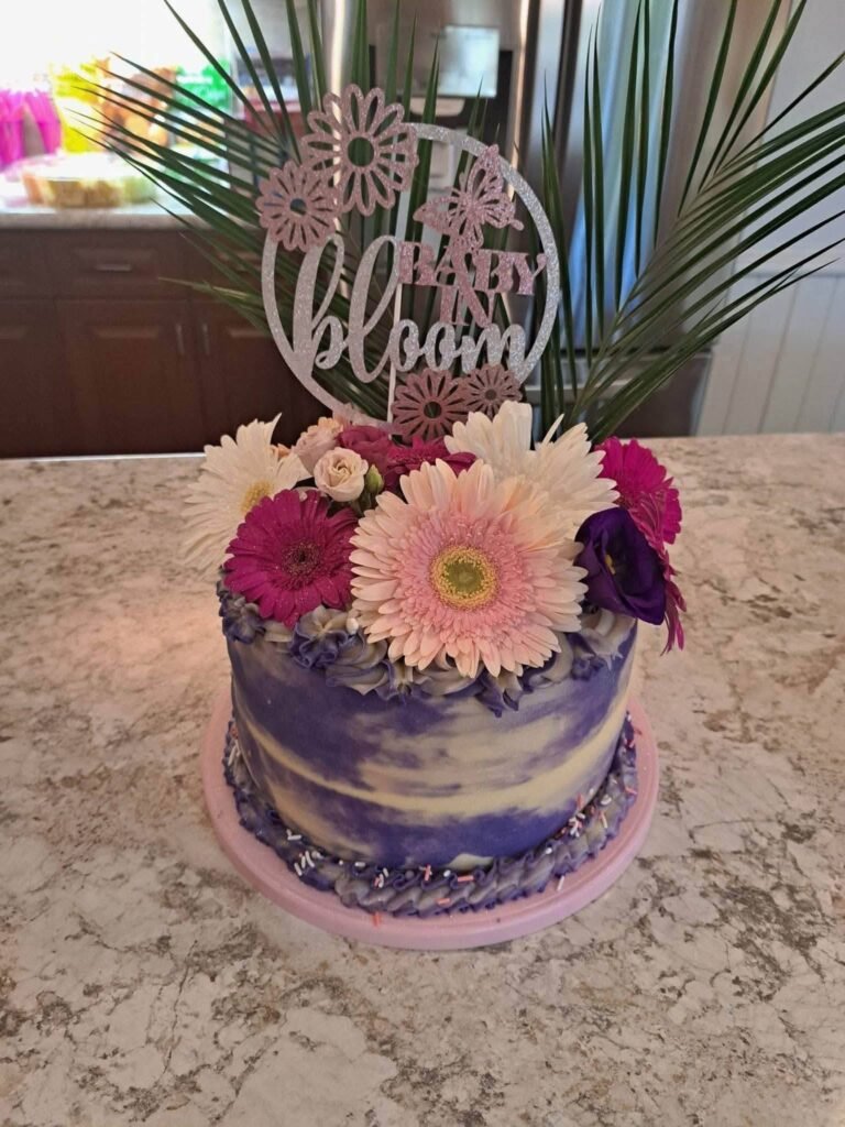 Purple watercolor baby shower cake with gerbera daisies and a Baby in Bloom topper