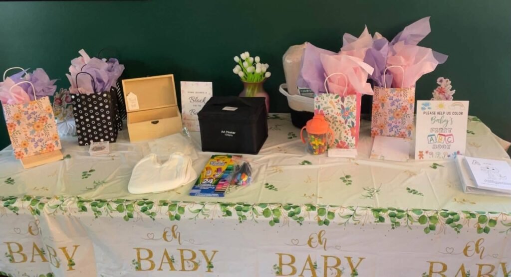 Baby shower gift table with gift bags and a card box on an oh baby tablecloth