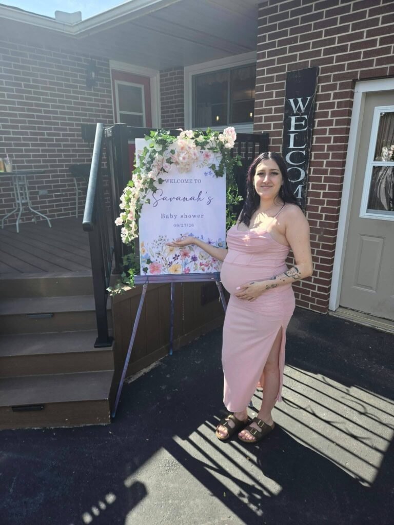 Mom to be in a pink bodycon dress with a side slit by a wildflower welcome sign