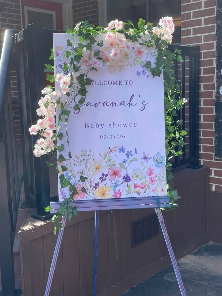 Baby shower welcome sign with wildflowers and faux pink blossoms on an easel