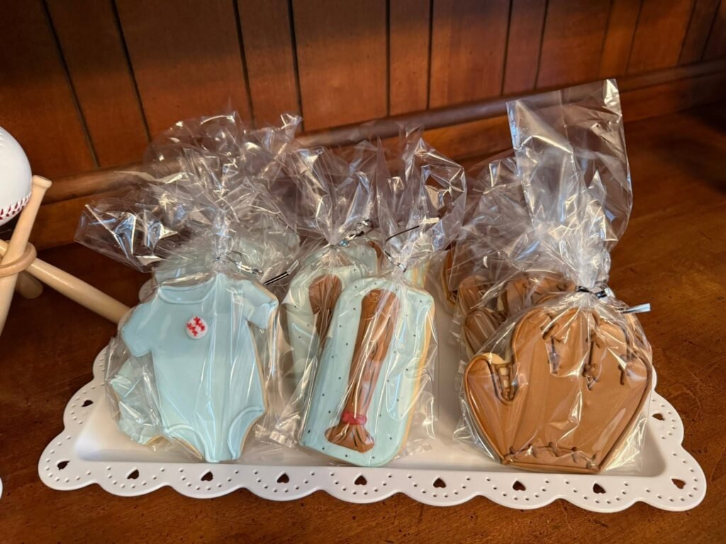 Baseball baby shower cookies shaped like a onesie, bat and glove in clear bags