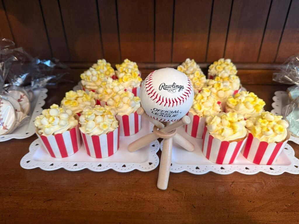 Popcorn cupcakes in red striped wrappers around a baseball on a stand