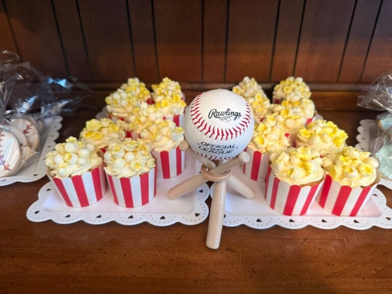 Popcorn cupcakes in red striped wrappers around a baseball on a stand