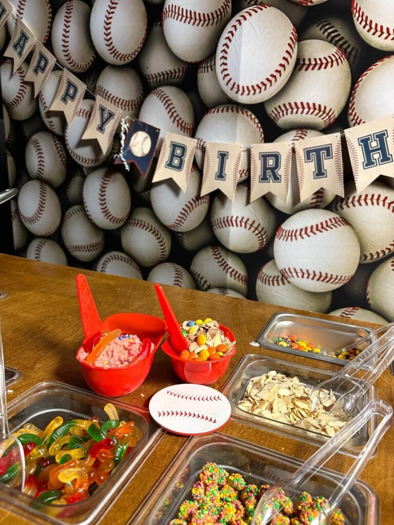 Happy Birthday banner on a baseball wall backdrop above a sundae topping bar