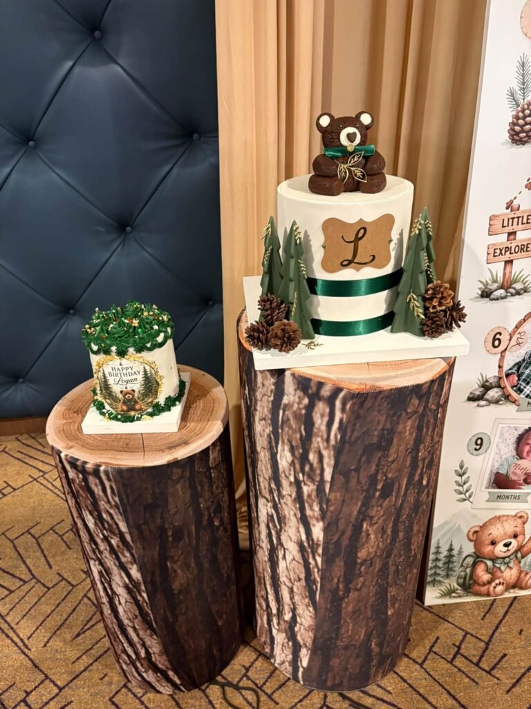 Teddy bear 1st birthday cake with pinecones and green ribbon on tree stump cake stands