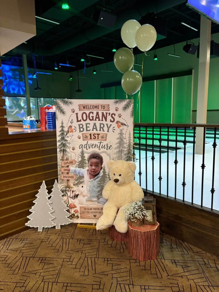 Teddy bear first birthday welcome sign with white wooden trees and a plush bear