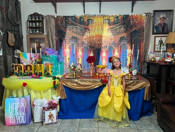 Birthday girl in a yellow Belle dress next to the Beauty and the Beast party table with red roses