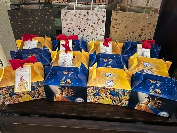 Blue and yellow Beauty and the Beast favor boxes with red bows lined up on a table