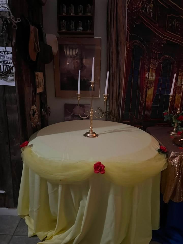 Round guest table with a yellow tulle overlay, a red rose and a gold candelabra in front of a ballroom backdrop