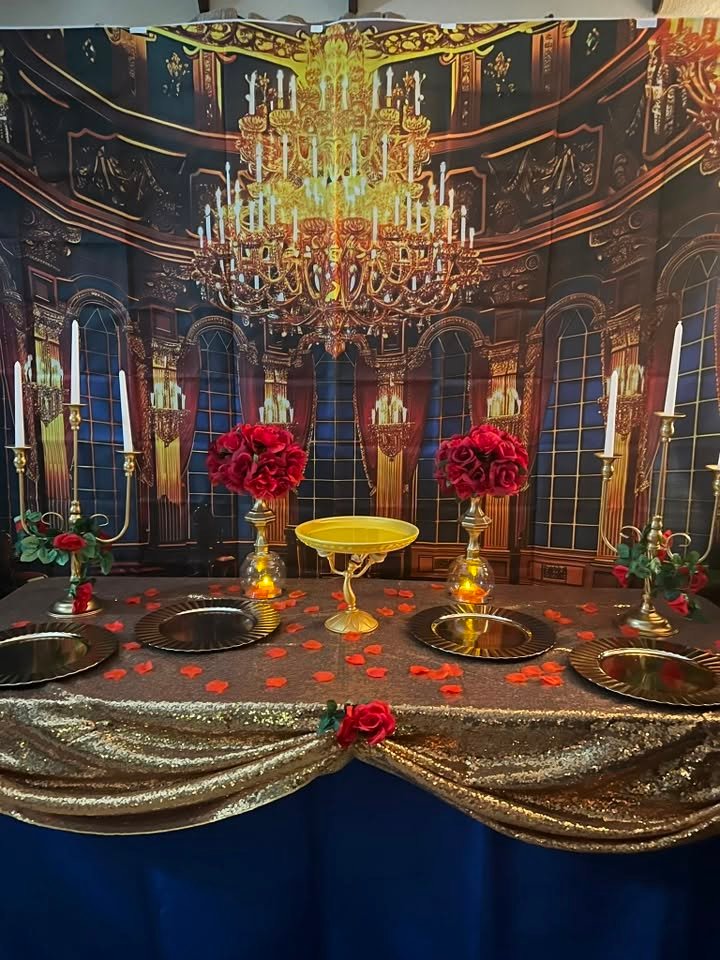 Beauty and the Beast dessert table with a ballroom backdrop, red roses, gold candelabras, gold chargers and a gold sequin cloth