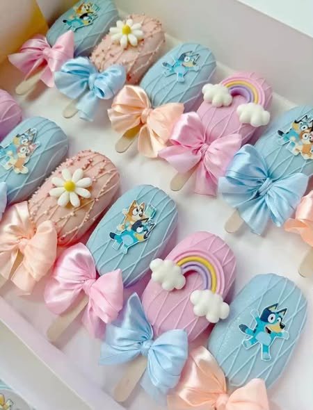 Pastel cakesicles with satin bows, fondant daisies, rainbows and Bluey toppers in a gift box
