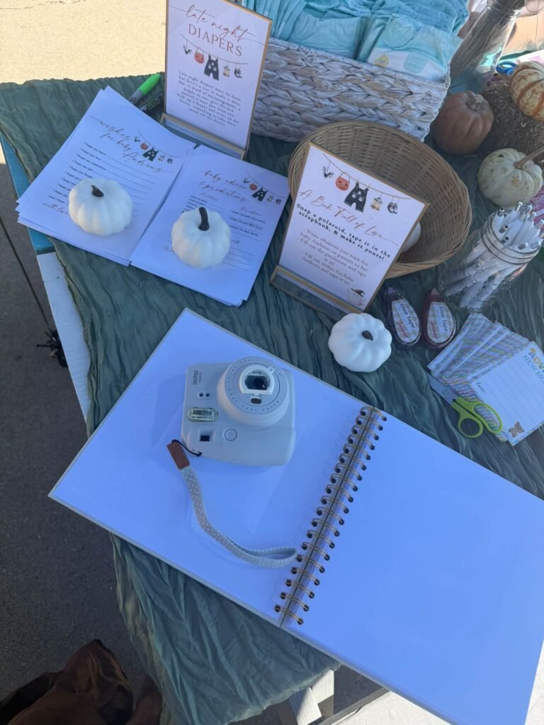 Baby shower guest table with an instant camera photo guest book, a late night diapers sign, advice cards and mini white pumpkins