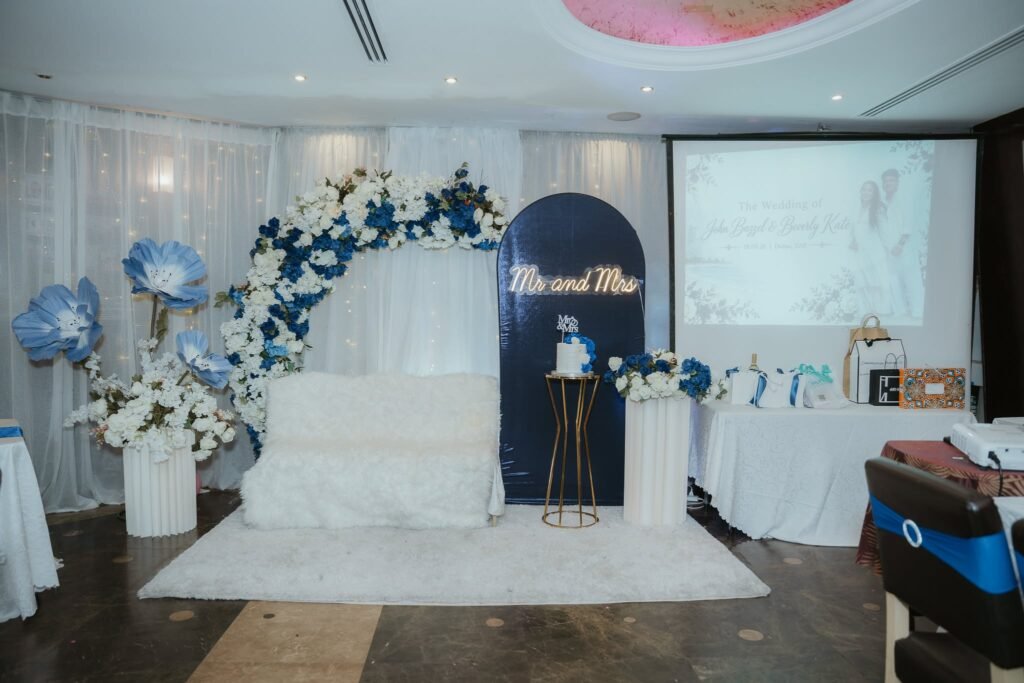 Blue and white wedding stage with a navy Mr and Mrs arch, flower arch, giant blue paper flowers and a white loveseat