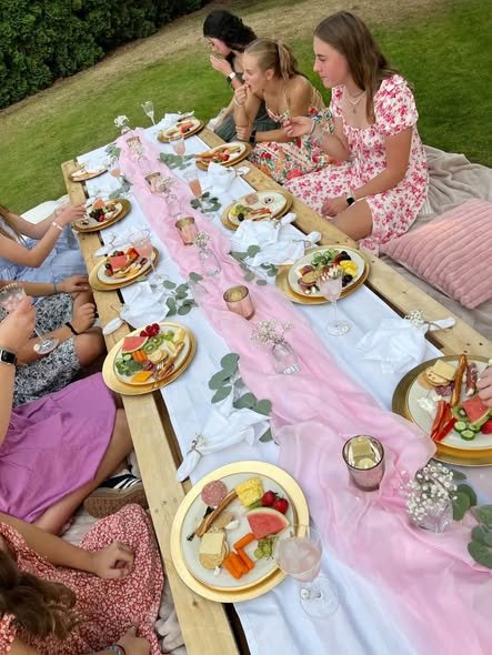 Guests sitting at a low picnic table with a pink runner and mini cakes