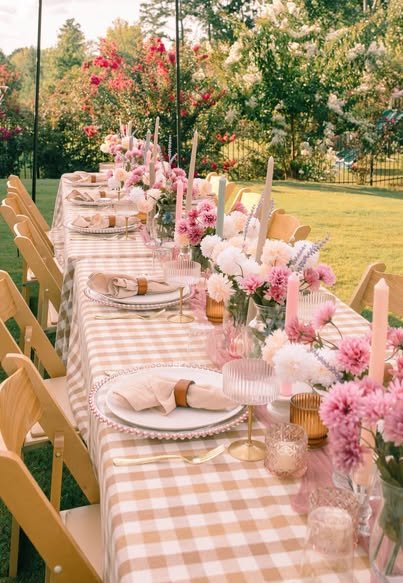 Long garden picnic table with a pink gingham cloth, pink flowers, candles and wooden folding chairs