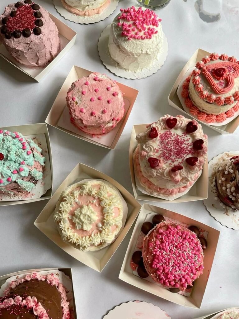 Mini cakes decorated with pink, red and green piping and berries on a white table