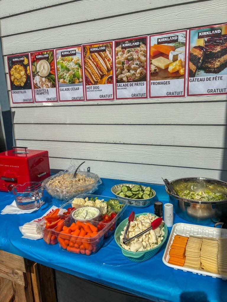 Costco party buffet with a food court menu sign, salads, veggie trays and snacks on a blue table