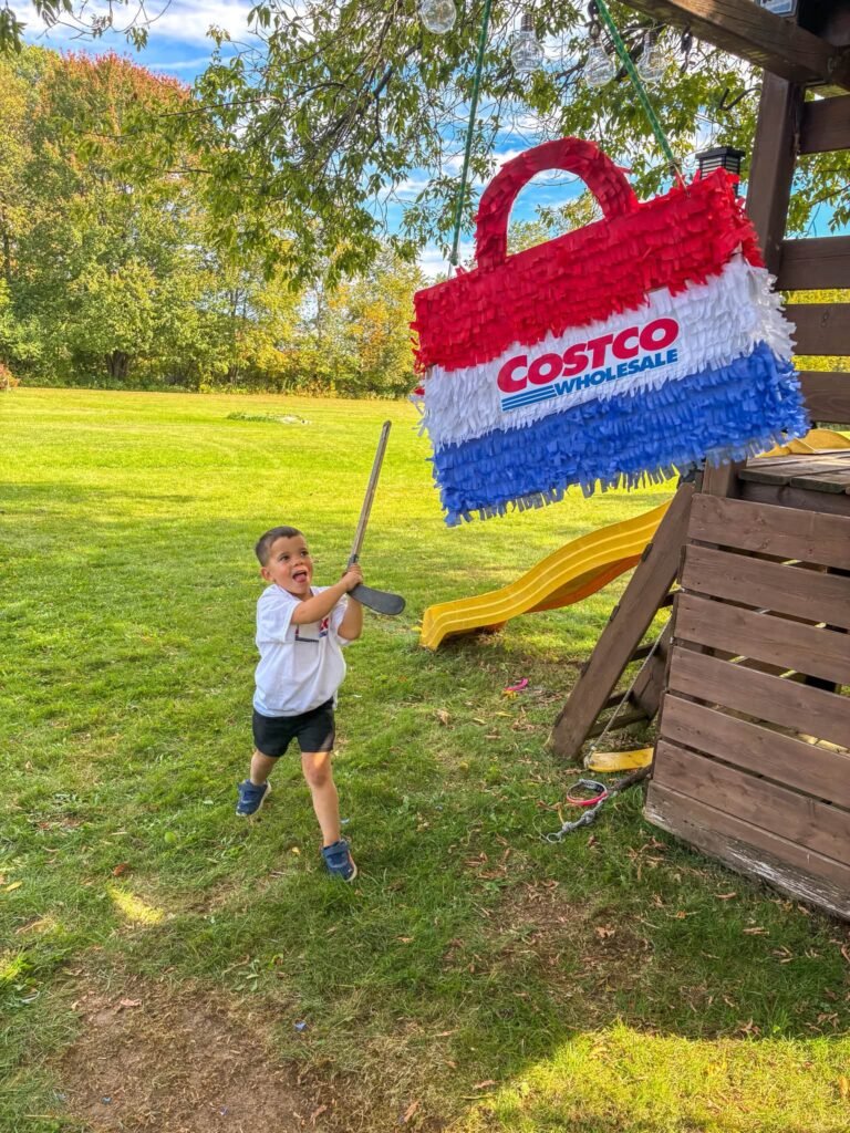 Kid hitting a red, white and blue Costco shopping bag pinata in a backyard