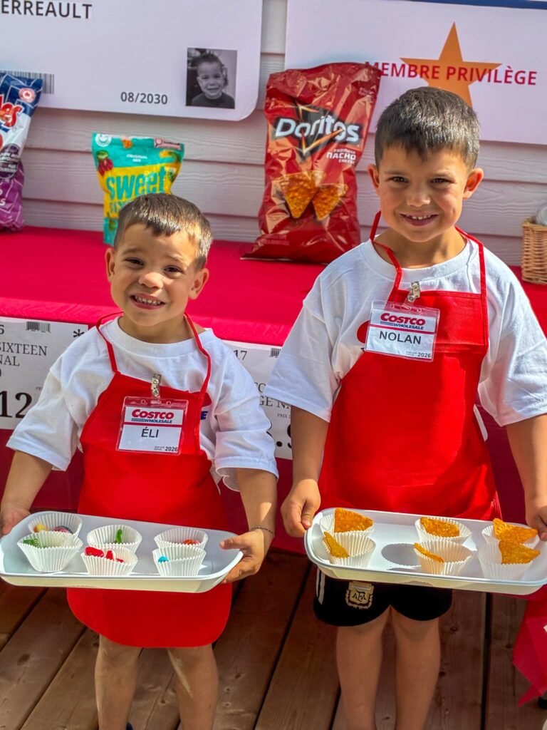 Two kids in red aprons with name tags holding snack sample trays