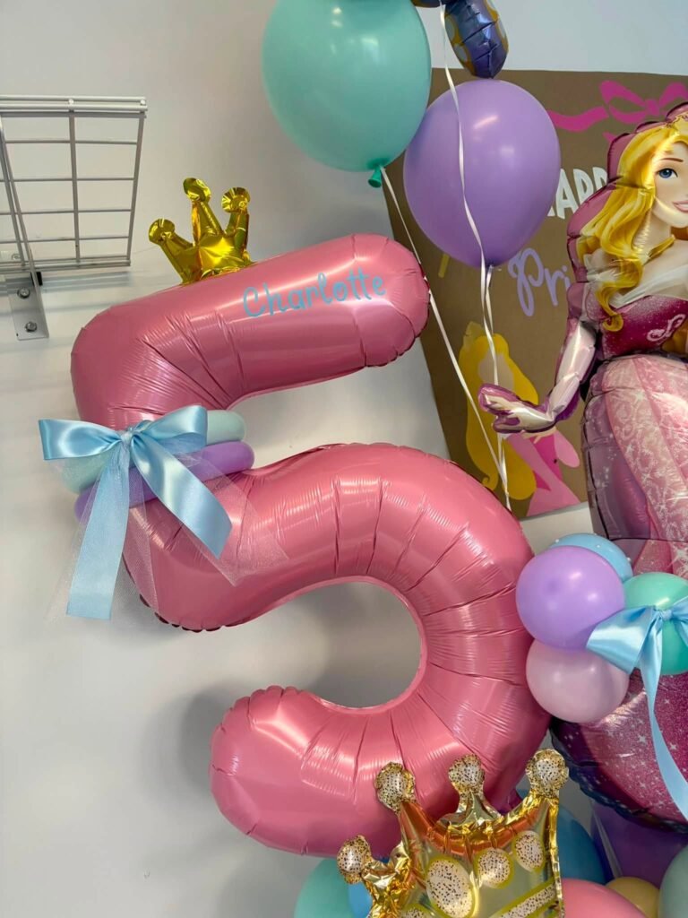 Close up of a pink number 5 balloon with gold crowns and a blue bow for a princess 5th birthday