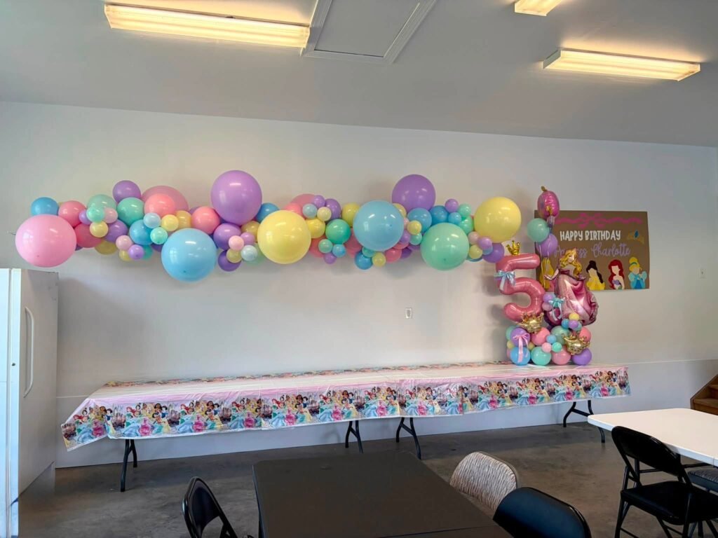 Long pastel balloon garland over a princess party table in a plain room