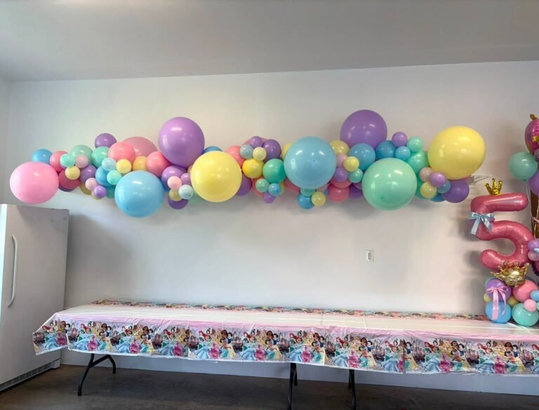 Long pastel balloon garland over a princess party table with a Happy Birthday banner