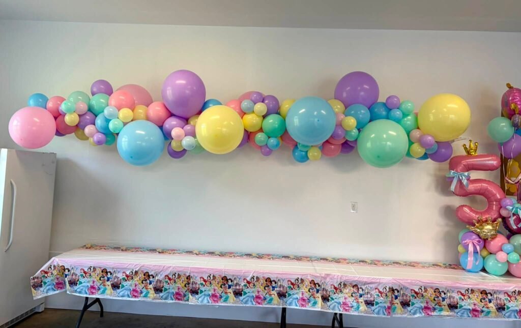 Wide view of a princess 5th birthday party room with a pastel balloon garland and number 5 balloon