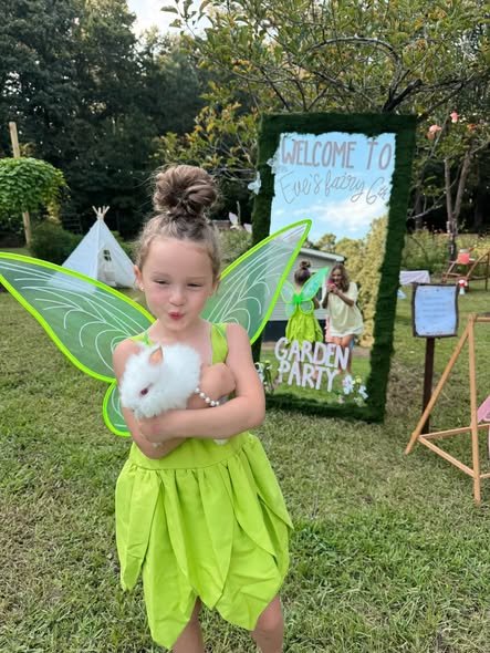 Girl in a green fairy costume with wings holding a toy bunny by the welcome sign