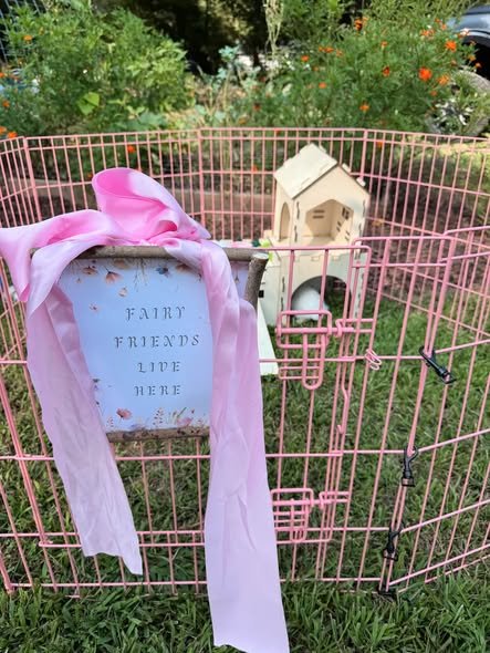 Fairy Friends Live Here sign with a big pink bow on a pink pet pen with a small wooden house in a garden