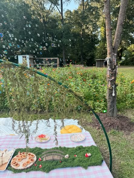 Fairy snack table with a pink gingham cloth, a faux grass runner with a tiny bridge and fairy snacks in a garden